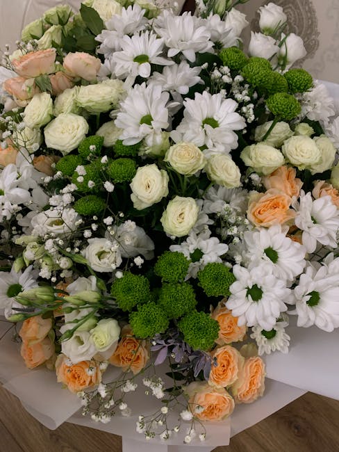 A large, lush floral bouquet featuring an assortment of fresh flowers arranged in a dense, rounded style. The bouquet includes white daisies with bright white petals and yellow centers, delicate white