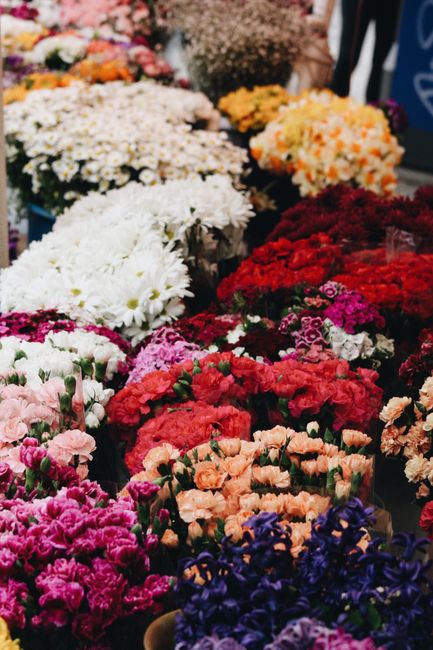 A vibrant display of fresh flowers at a market stall, featuring a variety of blooming blooms arranged in dense bouquets. The selection includes pink, white, red, purple, and orange flowers, with some